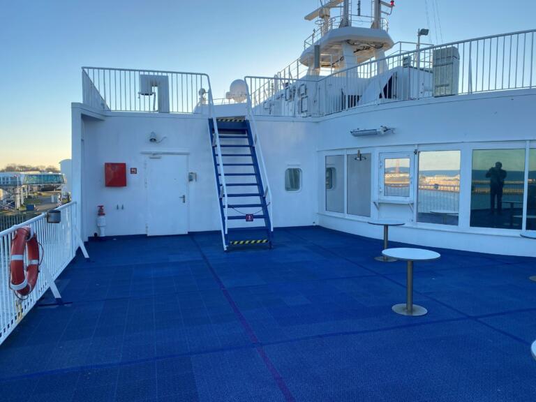 The sun deck of the ferry with its blue floor and stairs to the upper deck